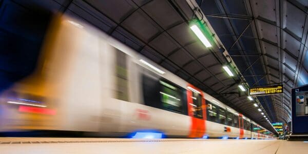 High-speed train arriving at a modern underground metro station with illuminated platform signs and a curved ceiling.